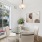 Bright dining area with a round glass table, four modern chairs, and large window views, accented by abstract wall art and a lush plant.